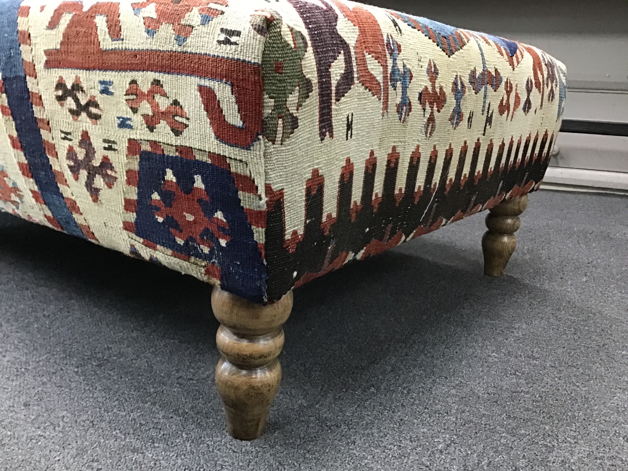 A large rectangular coffee table / footstool with antique kelim upholstery on stained turned beech feet, width 124cm, depth 72cm, height 38cm.